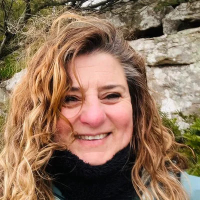 Retrato de Mony, sonriendo al aire libre, con campera celeste y cuello de polar negro